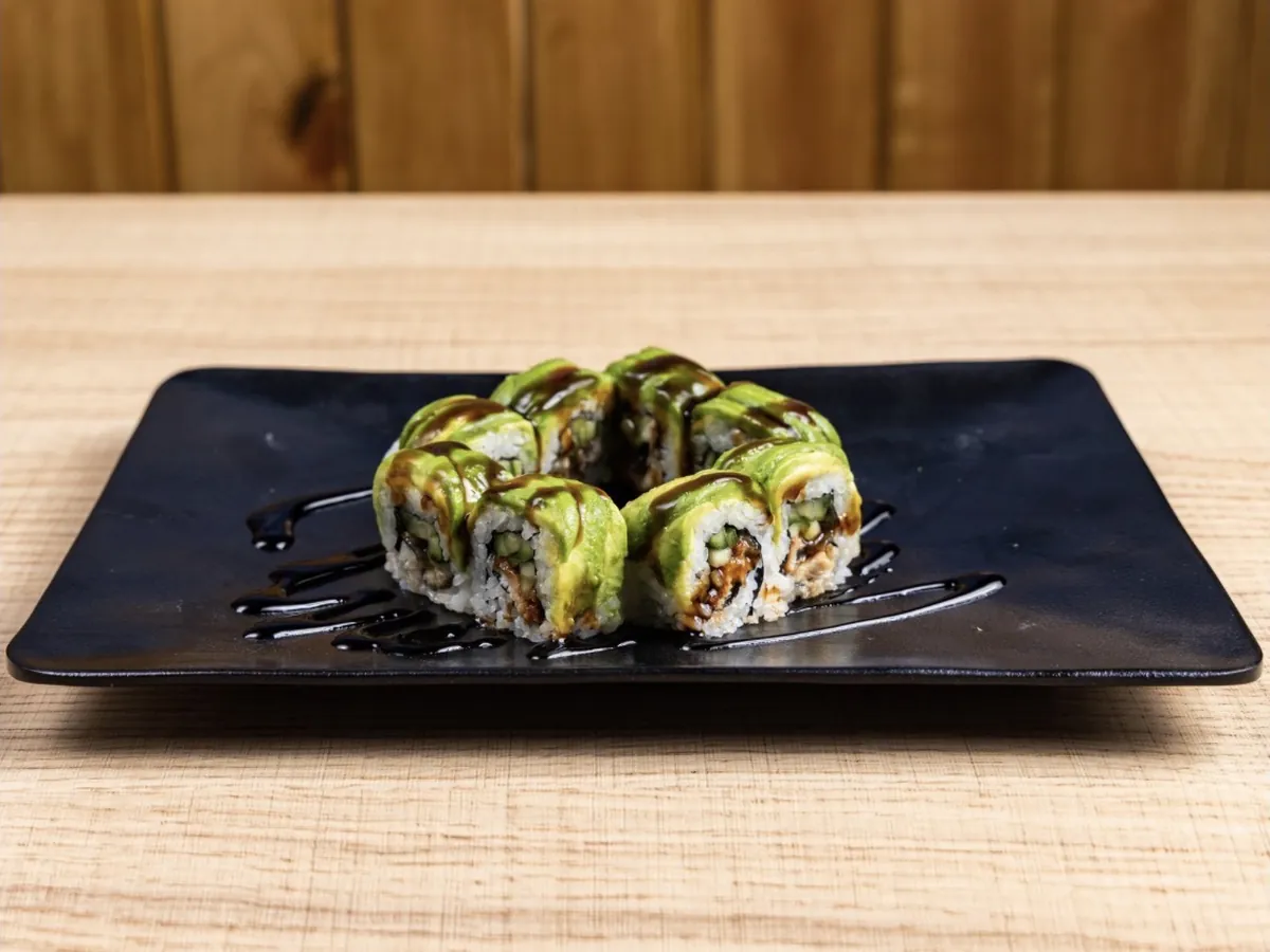 Green Dragon Roll draped in sliced avocado with eel sauce brushed across a black plate