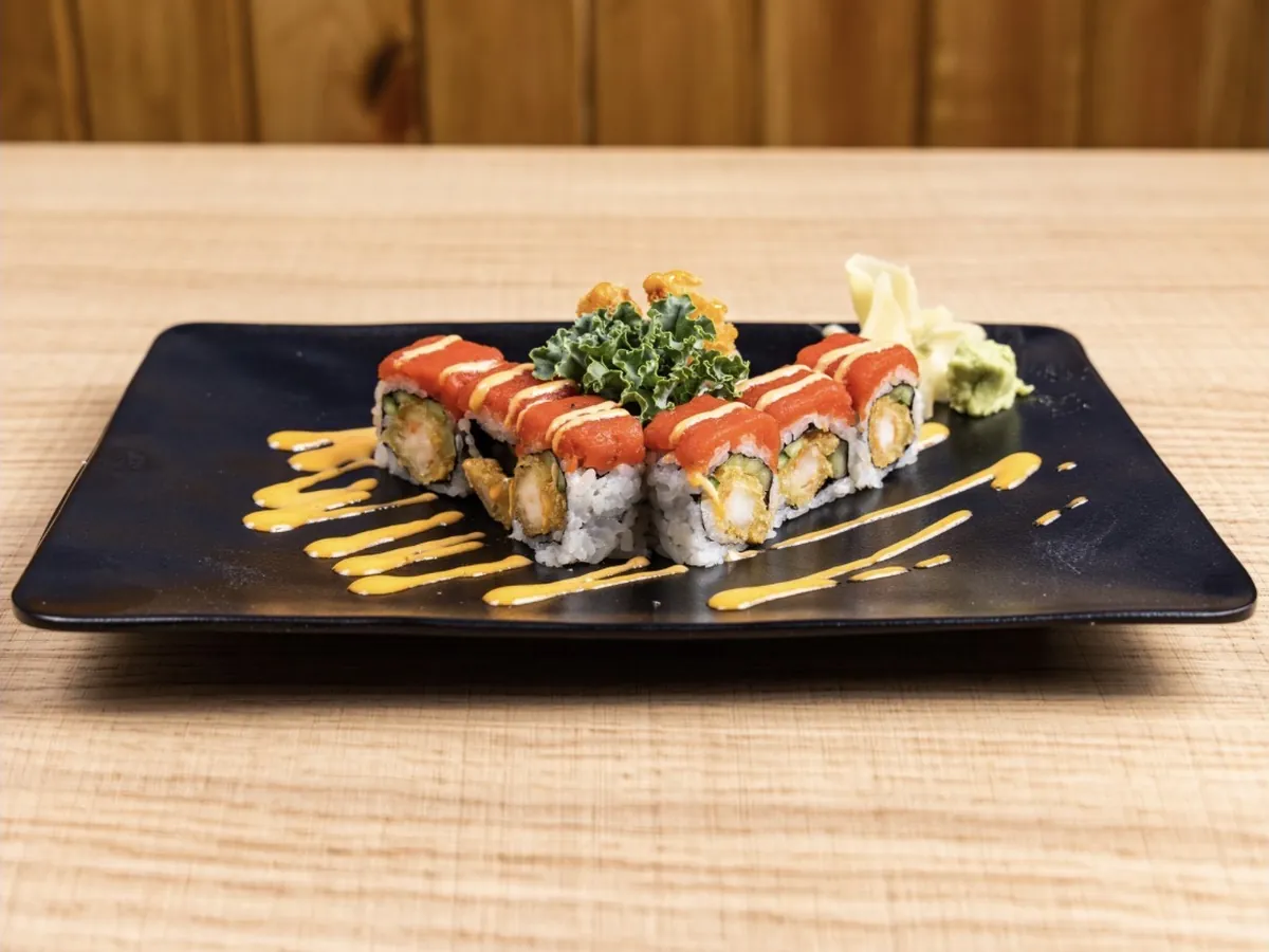 Phoenix Roll topped with spicy tuna and drizzled with spicy mayo, plated on black stoneware with kale