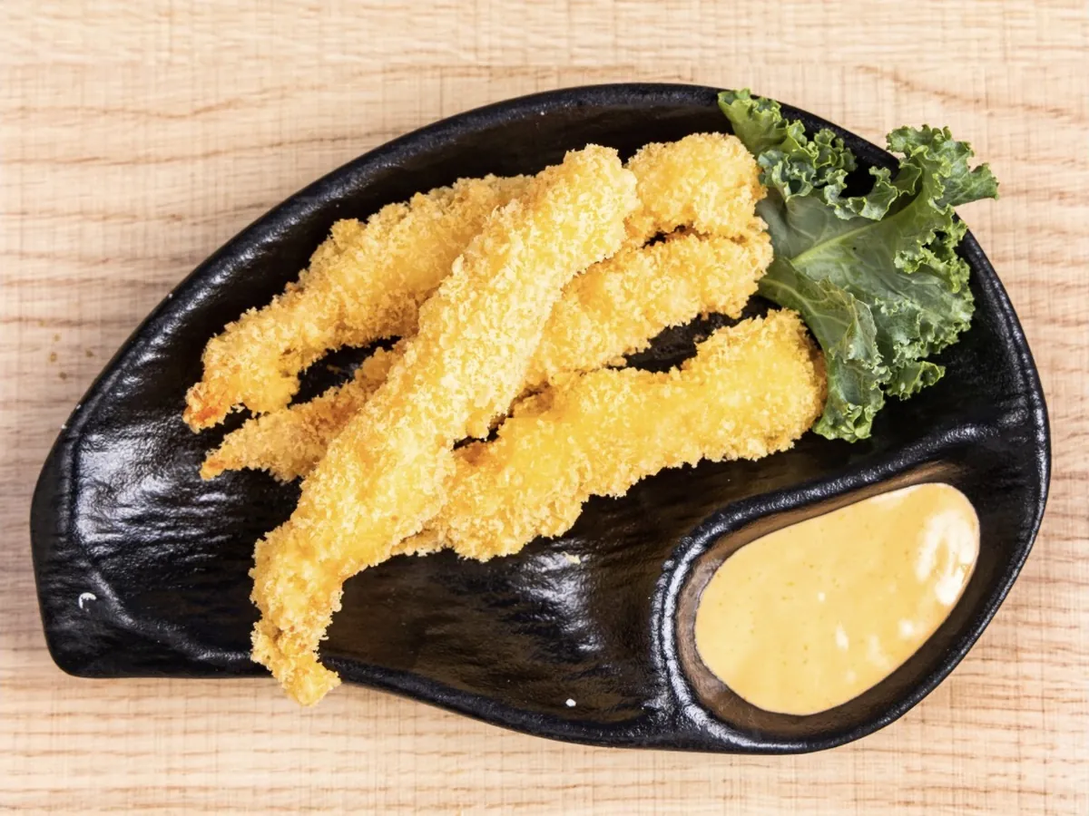 Shrimp tempura fried in panko, plated beside a pool of dipping sauce on a black dish