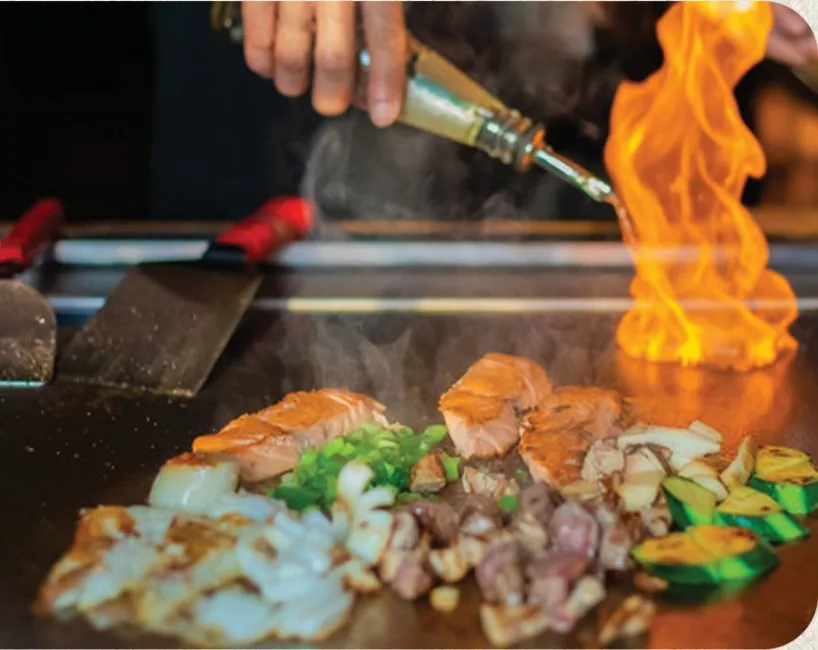 Hibachi chef searing salmon and vegetables over flame on the flat-top grill